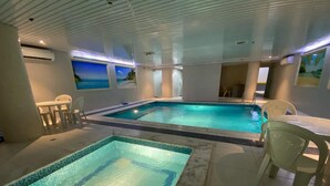 An indoor swimming pool with a tiled floor, a seating area with chairs, and a view of the sea through a window. - Royal Boutique Hotel (Khamis Mushait)