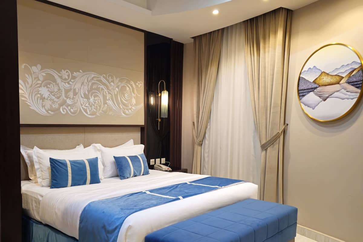 Un dormitorio moderno con una cama grande, una mesita de noche, una obra de arte en la pared y una lámpara en el techo.