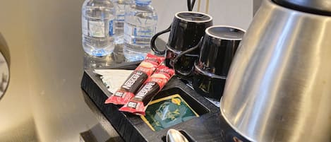 Un minibár con agua embotellada, tazas de café, una cafetera y una cuchara.