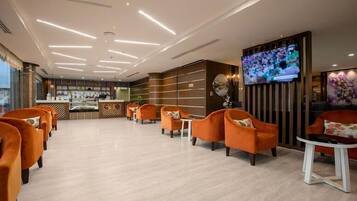 Een moderne lobby met oranje zitplaatsen, een receptiebalie en een groot televisiescherm.