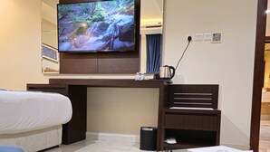 A hotel room with a bed, a desk with a TV, a coffee maker, and a remote control. - Royal Boutique Hotel (Khamis Mushait)