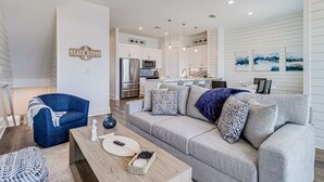 A modern living room with a grey sofa, a blue armchair, and a wooden coffee table. - Three-story townhouse with a balcony, two living areas, & a washer/dryer (Port Aransas)