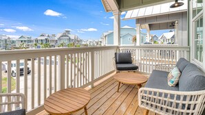 A covered outdoor area with a wooden deck, wicker furniture, and a view of neighboring houses. - Three-story townhouse with a balcony, two living areas, & a washer/dryer (Port Aransas)