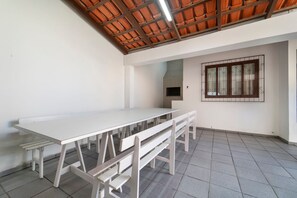 Une pièce avec une longue table blanche et des bancs, un sol carrelé, un plafond carrelé et une fenêtre avec des barreaux.