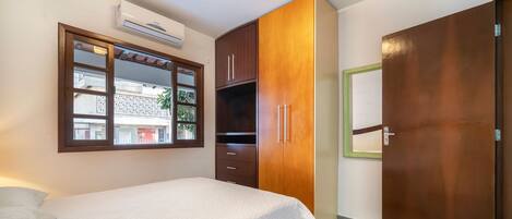A bedroom with a bed, a wardrobe, a window, and an air conditioning unit.