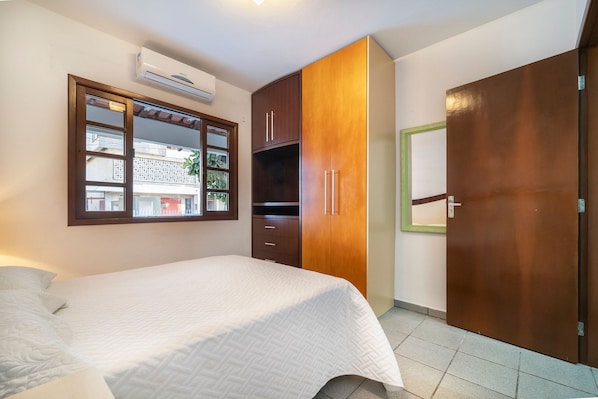 A bedroom with a bed, a wardrobe, a window, and an air conditioning unit.