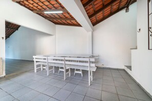 A room with a tiled floor, white walls, a wooden ceiling, and a white table with benches. - 914 - Casa 3 dormitórios para 8 pessoas (Bombinhas)