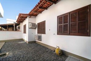 A building with a tiled roof, wooden shutters, and an air conditioning unit. - 914 - Casa 3 dormitórios para 8 pessoas (Bombinhas)