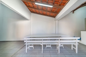 Een kamer met een grote witte tafel en banken, een betegelde vloer en een houten plafond met zichtbare balken.