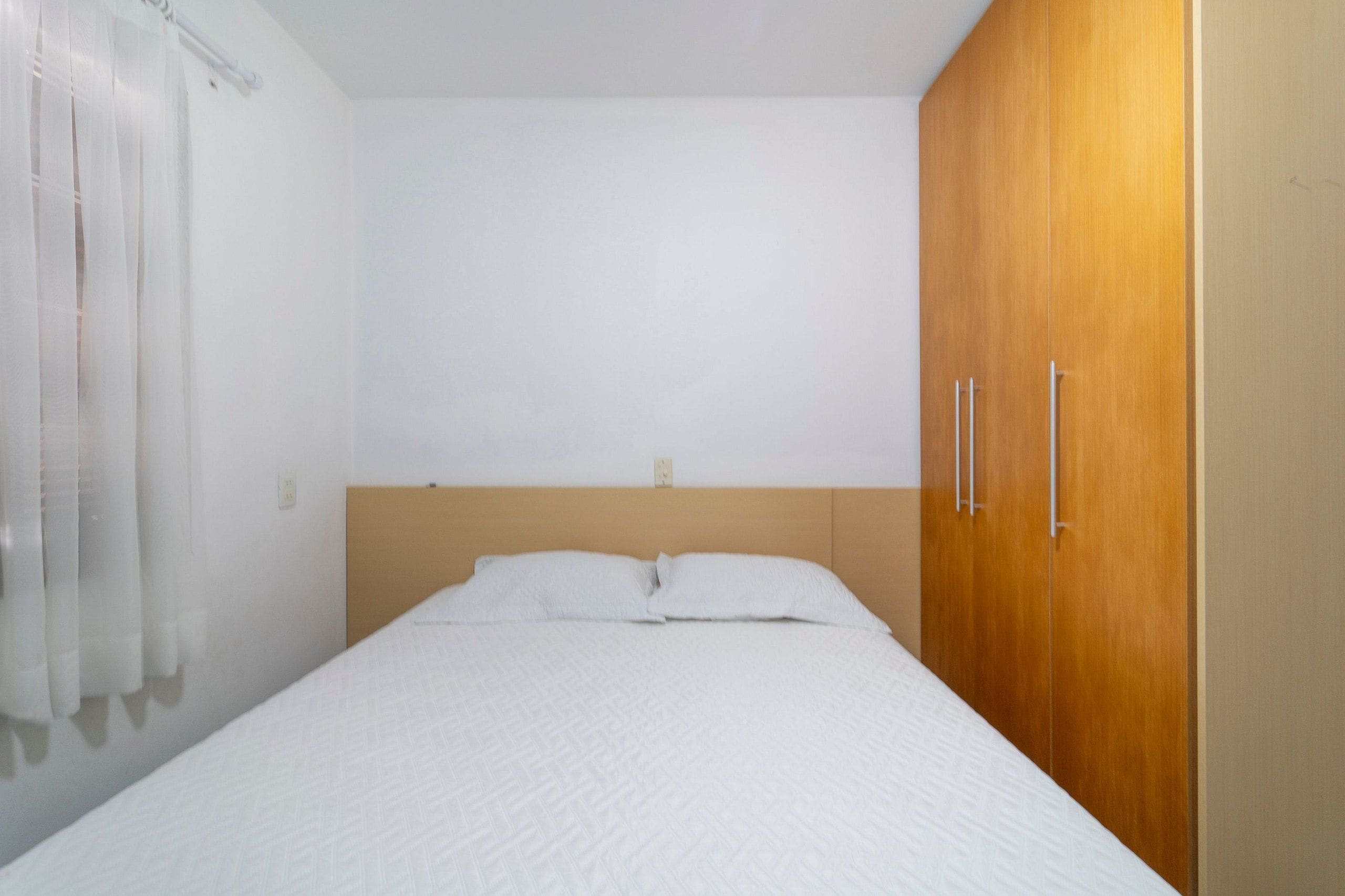 Une chambre à coucher avec un lit, une armoire en bois et un rideau blanc.
