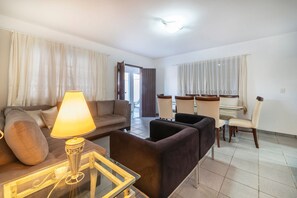 A living room with a sofa, armchair, lamp, and dining area with chairs and a table. - 914 - Casa 3 dormitórios para 8 pessoas (Bombinhas)