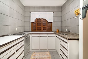 A compact kitchen with white cabinets, a built-in stove, a window with a curtain, and a granite countertop.