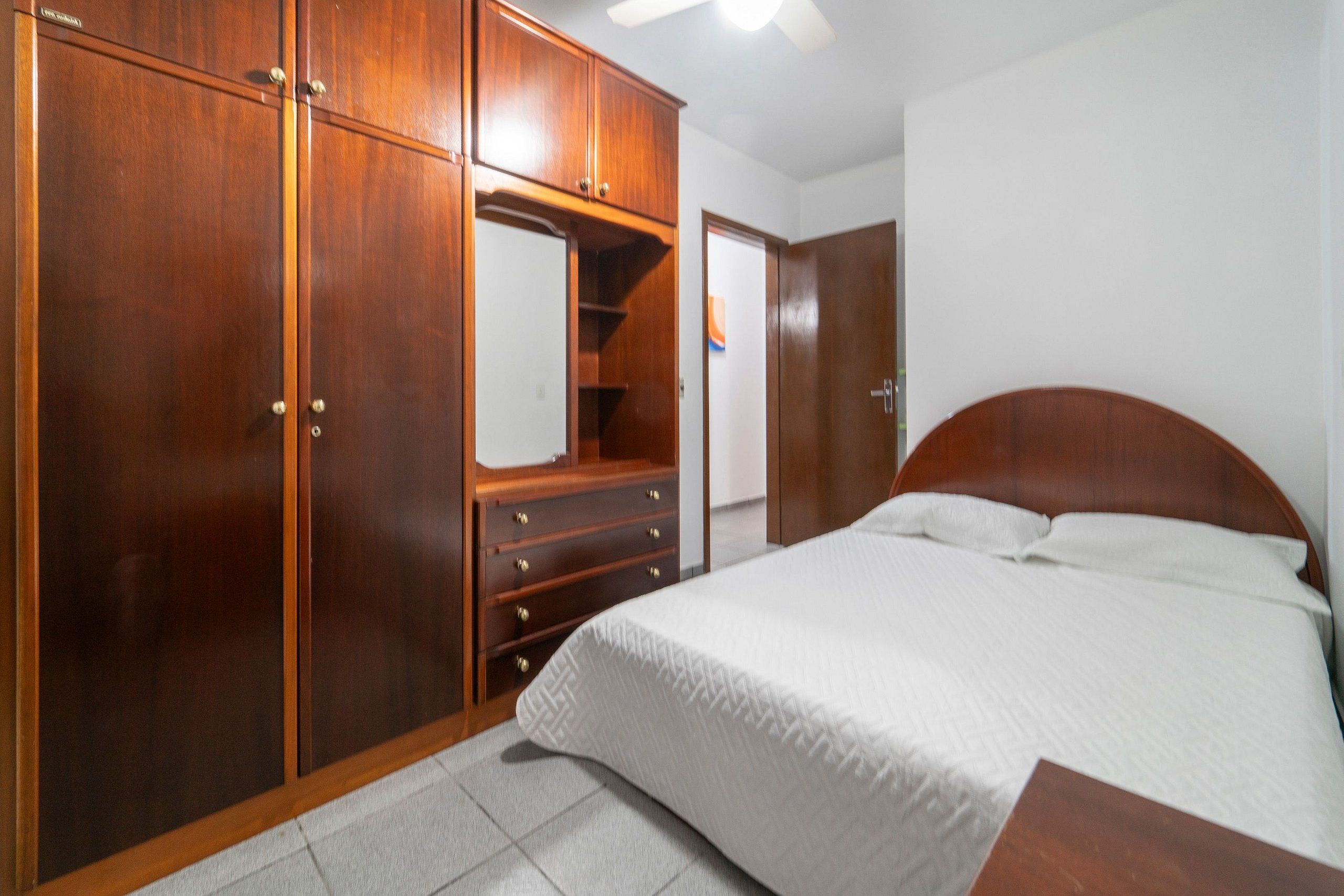 Quarto com guarda-roupa de madeira, cama e cómoda.