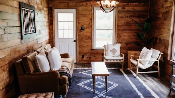 Una habitación acogedora estilo cabaña, con paredes de madera, un sofá, dos sillones, una mesita y una alfombra.