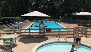 A swimming pool with lounge chairs and umbrellas, surrounded by a fence.