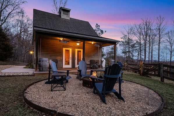 A wooden cabin with a covered porch, outdoor seating, and a fire pit.