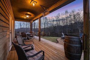 A wooden deck with outdoor seating, a large barrel, and a view of a forested area.
