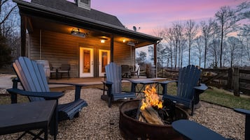 A wooden cabin with a covered patio, outdoor seating, and a fire pit.