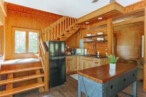 A wooden cabin interior with a kitchen, a dining area, and a staircase.