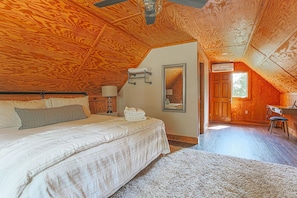 A bedroom with a wooden ceiling, a bed with a white comforter, a bedside table with a lamp, and a mirror on the wall.