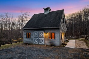 Une cabane rustique avec un toit à pignon abrupt, une cheminée et un porche à l’avant.