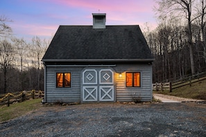 A small, single-story house with a dark roof and light siding, featuring a central door with diamond-shaped windows and a small attic vent.