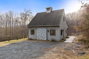 A small, single-story building with a sloped roof and a chimney, surrounded by a gravel driveway and a wooden fence.