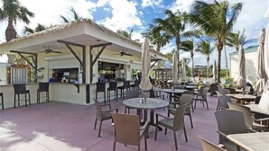 Een terras met tafels, stoelen, een bar en palmbomen.