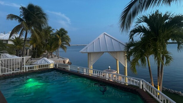 A pool area with a clear view of the sea, surrounded by palm trees and a gazebo. - Beautiful Open-Water Property (Big Pine Key)