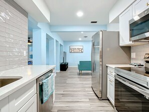 Une cuisine moderne avec des armoires blanches, un réfrigérateur en acier inoxydable et un plancher en bois.