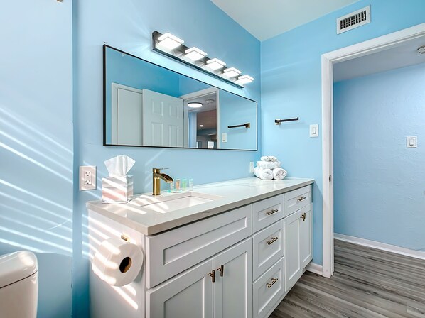 A bathroom with a white vanity, a large mirror, and a towel stack.