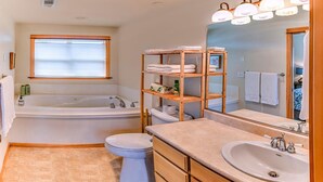 A bathroom with a bathtub, toilet, vanity with sink, and shelves with towels. - 2-story, 3 bedroom modern home with king and queen beds, living room and kitchen. (Ashland)