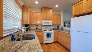 A kitchen with wooden cabinets, a white stove, a microwave, a sink, and granite countertops. - 2-story, 3 bedroom modern home with king and queen beds, living room and kitchen. (Ashland)