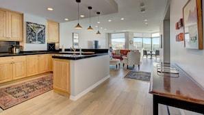 Cocina amplia con armarios de madera, una isla central, iluminación colgante y vistas a una sala de estar con sofá y sillones.