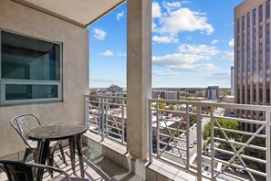 A balcony with a table and chairs, a window, and a view of the cityscape.