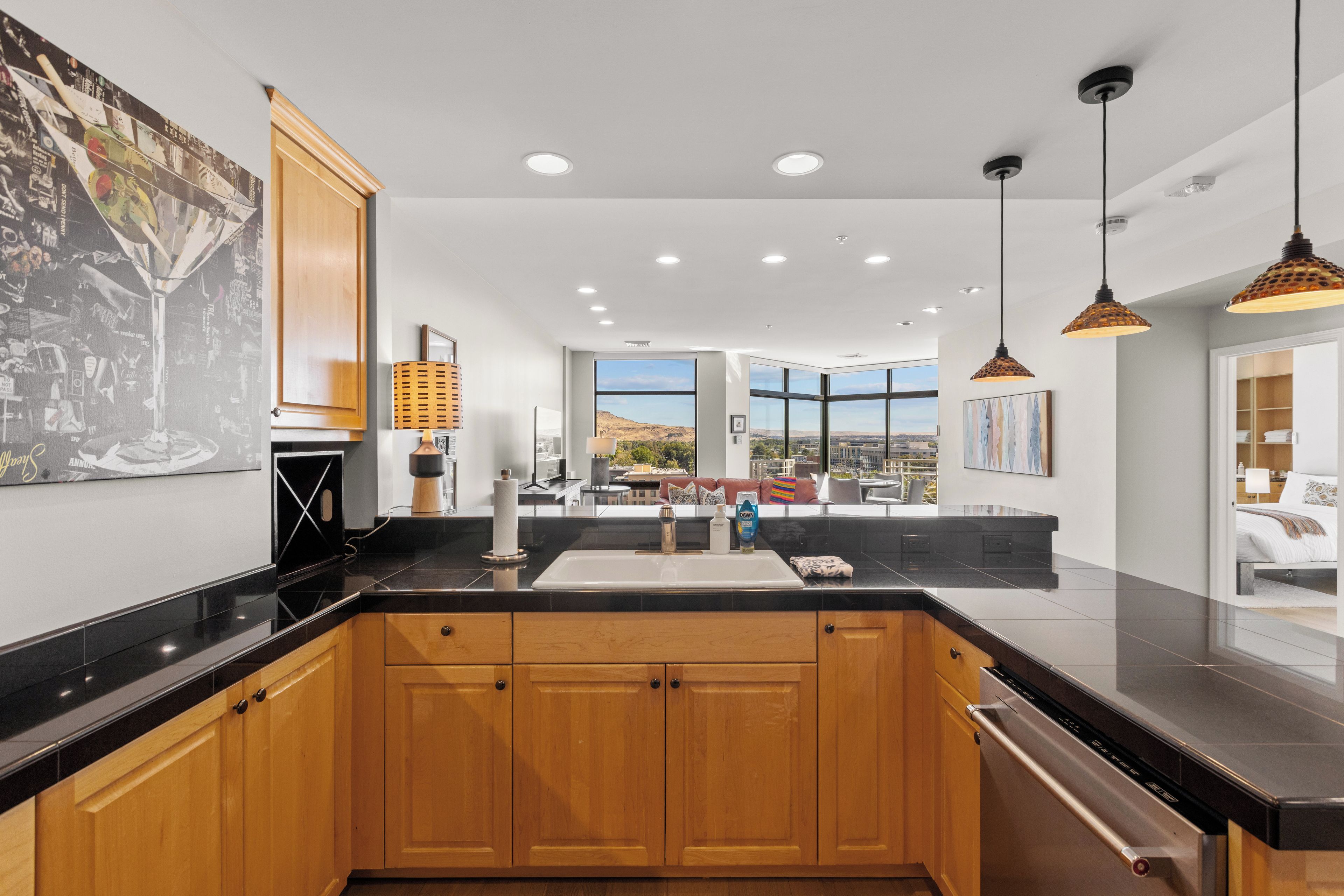 A modern kitchen with wooden cabinets, a black countertop, and a view of the cityscape through large windows.