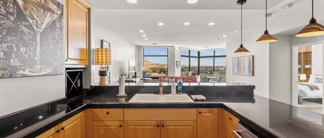 A modern kitchen with wooden cabinets, a black countertop, and a view of the cityscape through large windows.