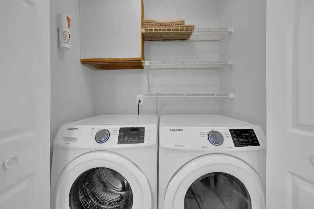 A laundry area with two Samsung washing machines and a wall-mounted heater.