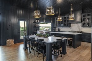 A modern kitchen with a large island, dark wood paneling, and pendant lighting. - Favorite Luxury Cabin w stunning views 3 level Deck- sauna/Hot Tub/putting green (Broken Bow)