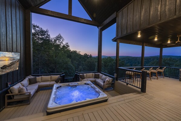 A wooden deck with a hot tub, a sofa, and a dining table. - Favorite Luxury Cabin w stunning views 3 level Deck- sauna/Hot Tub/putting green (Broken Bow)