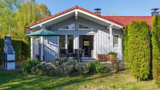 Een huis met een rood dak, een witte gevel en een overdekte patio met tuinmeubilair.
