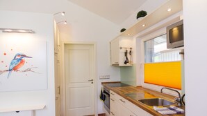 Een kleine keuken met witte kastjes, een houten aanrecht, een ingebouwde oven en een raam met jaloezieën.