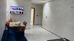 A modern living room with a flat-screen TV mounted on the wall, a dining table with chairs, and a blue sofa. - Les Belles Residences F (Tangier)