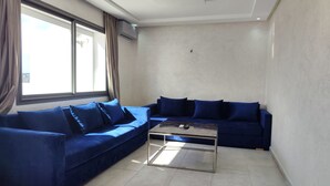 A modern living room with two blue sofas, a glass coffee table, and a large window with curtains. - Les Belles Residences F (Tangier)