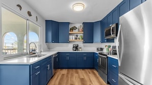 A modern kitchen with blue cabinets, stainless steel appliances, and a wooden floor.