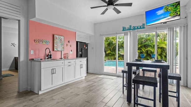 A modern kitchen with white cabinets, a pink accent wall, and a large window overlooking a pool.