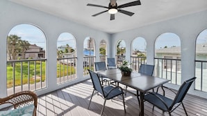 A covered patio with a table and chairs, large arched windows, and a ceiling fan.