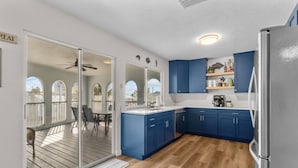 A modern kitchen with blue cabinets, a refrigerator, and a sliding glass door leading to an outdoor deck.