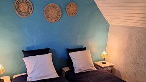 A room with two beds, a blue accent wall, and three woven wall hangings.