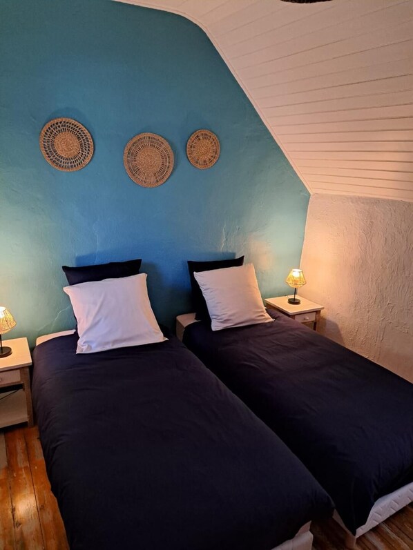 Une chambre avec deux lits, un mur d’accent bleu et trois décorations murales tissées.